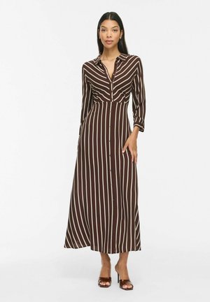 Femme portant une robe midi à manches longues boutonnée, rayée verticalement marron et blanche, avec un col et des talons ouverts marron.