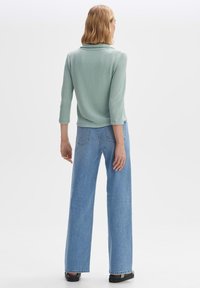 Mynta grön, texturerad tröja med krage; kombinerad med ljusblå, vida jeans. Modellen bär svarta klackskor.