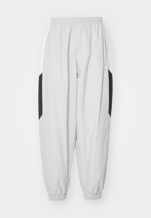 Pantalones de chándal ligeros en gris claro, fabricados con material ligero, con cintura y puños elásticos, y paneles laterales en negro y blanco contrastantes.