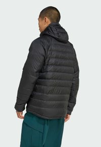 Padded black jacket with a hood, featuring a quilted design and smooth texture. The model wears green cargo pants, viewed from the back.
