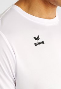 Witte sportshirt met een gladde textuur, met een ronde halslijn en het zwarte "erima" logo op de bovenste voorkant.
