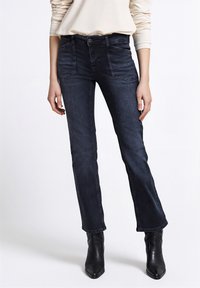 Tmavě modré džíny z denimu s úzkým st�řihem, vybavené předními kapsami, zapínáním na knoflíky a jemnými detaily šití, doplněné černými kotníkovými botami.
