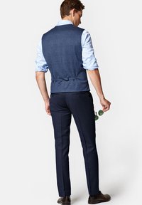 Granatowa kamizelka w kratę noszona na jasnoniebieskiej koszuli, w połączeniu z wąskimi granatowymi spodniami i ciemnobrązowymi skórzanymi butami.