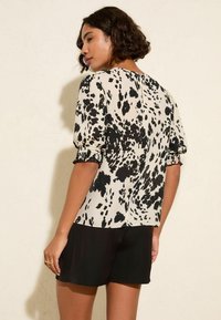 Blusa in stampa animale bianco e nero con maniche a sbuffo, polsini arricciati e chiusura con bottone sul retro, realizzata in un tessuto morbido e leggero.