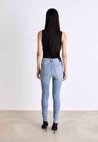 Tunna blå denimjeans med en urtvättad finish, hög midja och bakfickor, i kombination med en figurnära svart ärmlös topp och högklackade skor.