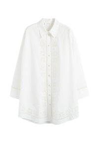 Camicia di cotone bianca con chiusura a bottoni, dettagli floreali ricamati lungo il sottopunto e l'orlo, e colletto classico. Maniche lunghe e ampie.