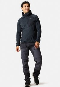 Zwarte, zip-up jas met een capuchon en contrasterend schouderpaneel; gecombineerd met grijze, met rits gesloten broek met cargozakken en versterkte naden.