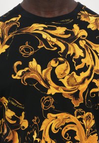 Svart t-skjorte med utsøkte gyldne blomsterdesign. Mønsteret inkluderer svevende motiver og teksturerte aksenter for et dristig utseende.