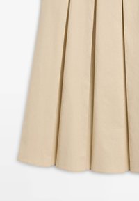 Beige plisseret nederdel lavet af glat stof med brede, skarpe folder og en ren kant.