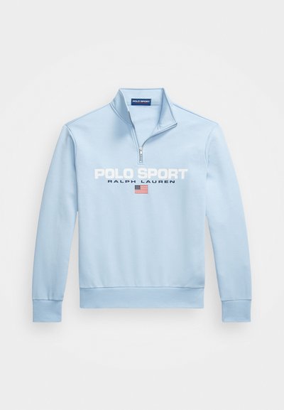 Jasnoniebieska bluza z zamkiem na szyi i długimi rękawami. Zawiera białe napisy "POLO SPORT" oraz "RALPH LAUREN", wraz z detalem amerykańskiej flagi.