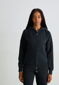 Moleton preto com fecho na frente em tecido suave, com mangas raglan, bolsos frontais e capuz. Apresenta detalhe do logótipo no peito e punhos canelados.