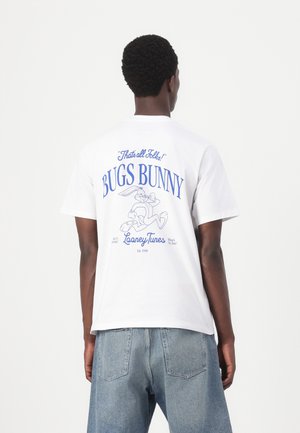 T-shirt en coton blanc avec une impression graphique de Bugs Bunny au dos. Le texte comprend "C'est tout, mes amis !" et "Looney Tunes" en bleu.