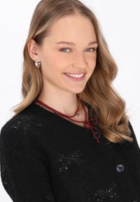 Maglione nero lavorato a maglia con collo rotondo e chiusura a bottone; decorato con delicati scintillii. Collana di perle rosse con un piccolo ciondolo a forma di cuore. Orecchini in argento.