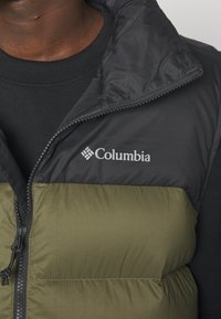 Mężczyzna ubrany w czarną i oliwkowozieloną pikowaną kamizelkę Columbia na czarnym t-shircie z okrągłym dekoltem, widoczny od klatki piersiowej do szyi.