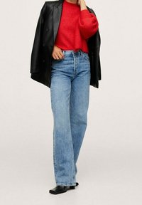 Jean large bleu clair associés à un pull texturé rouge et une veste en cuir noire, complétés par des chaussures à talons blocs noires.