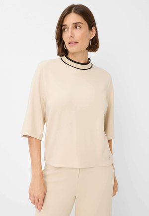 Beige t-shirt met korte mouwen en een ronde halslijn, met een contrasterende zwarte bies. Zachte, gladde stof met een relaxte pasvorm en een minimalistisch ontwerp.