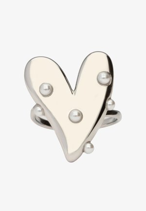Bague en forme de cœur en argent décorée de petites perles rondes sur un fond blanc uni.