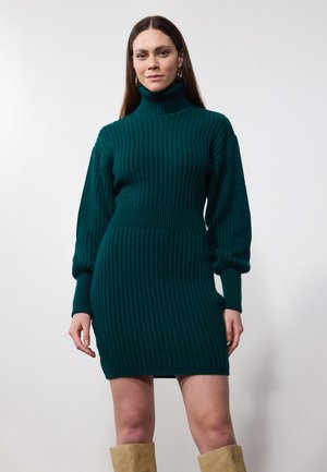 Grønn ribbestrikket kjole med høy polokrage, ballongsleeves og innsvingt midje. Knelengde med teksturert overflate.