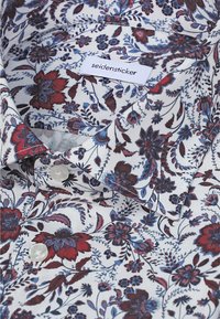 Chemise blanche avec motif floral rouge et bleu et une étiquette indiquant "seidensticker" sur le col.