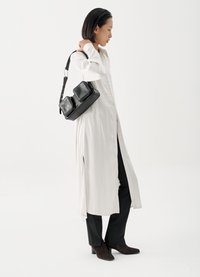 Λευκό μακρύ πουκάμισο με κουμπιά, μαύρη τσάντα με δύο θήκες, μαύρο παντελόνι και καφέ μπότες με τακούνι. Λεπτό ύφασμα με ανοίγματα στα πλάγια.