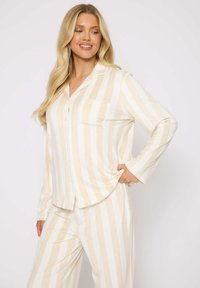 Leichtes, gestreiftes Pyjama-Set in Creme und Beige mit langen Ärmeln. Das knöpfbare Hemd verfügt über eine Brusttasche; die Hose hat eine lockere Passform.