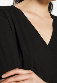 Sort V-hals t-shirt lavet af letvægtsstof, med korte ærmer og en afslappet pasform. Glat tekstur med minimal syning.