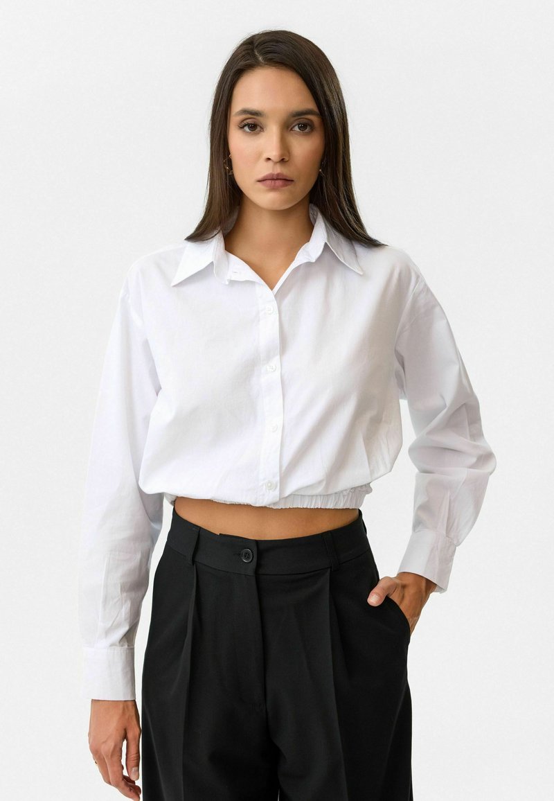 Witte geknipte button-up shirt met lange mouwen en een puntige kraag, gecombineerd met hoge zwarte broek met een voorzak.
