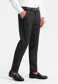 Pantalons noirs ajustés en tissu lisse, avec une coupe slim, des poches latérales et une taille épurée, associés à des mocassins noirs.