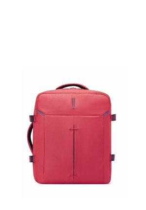 Red square-shaped backpack with top handle, side straps, and vertical seam details on front, standing upright on white background.