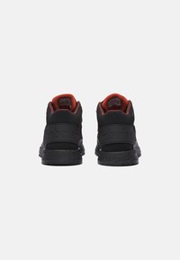 Czarne sneakersy z teksturowanym materiałem, gumową podeszwą i czerwonymi akcentami wewnątrz kołnierza. Posiadają wytłoczone logo na piętach.