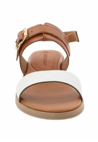 Sandalo in pelle marrone con una fascia bianca frontale, cinturino alla caviglia regolabile e suola piatta color sabbia. Design minimalista con accessori dorati.