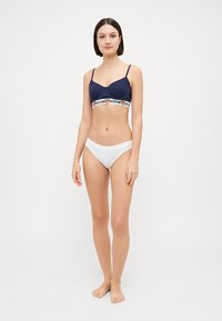 Navy bralette with thin straps and a white band featuring a logo; paired with white bikini briefs. Simple design and smooth texture.