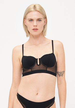 Zwarte beha met beugel, doorschijnende gaasdetails, verstelbare straps en een sleutelhoefontwerp. Zachte textuur en subtiele glans.