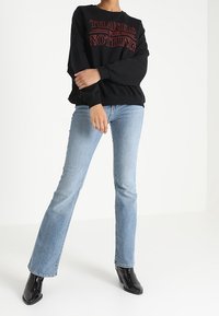 Czarna bluza z napisem "DZIĘKUJĘ ZA NIC" w czerwonym kolorze, w połączeniu z jasnoniebieskimi spódnicami o rozszerzanym kroju i błyszczącymi czarnymi botkami za kostkę.