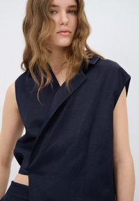 Mörkblå ärmlös topp med en inslagningsteknik, som har en skuren krage, en mjuk, lätt textur och sidodetaljer för en modern stil.