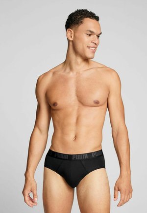 Schwarze Baumwollslips mit tailliertem Design und elastischem Bund, der das Puma-Logo in einem sich wiederholenden Muster zeigt, Modell seitlich dargestellt.