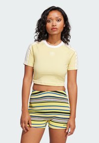 Light yellow cropped t-shirt with white stripes on sleeves, paired with multicolored striped shorts in yellow, blue, black, and pink.