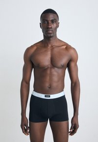 Sorte boksertruser med en kontrasterende lys grå midje, som har et logo. Stoffet ser glatt ut med en tettsittende design.