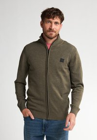 Olivgrüner Reißverschluss-Pullover mit hohem Kragen, gerippten Bündchen und Saum, mit einem kleinen schwarzen Logopatch auf der linken Brust.