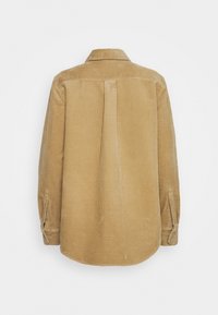 Camisa de pana en tono marrón claro, con mangas largas, cuello y un pliegue en la parte posterior. Presenta puños abotonados y una tela texturizada con canalones.