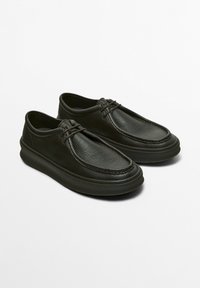 Chaussures noires en cuir à enfiler avec une surface texturée, un bout rond et une semelle épaisse noire. Présente un design de lacets minimal et des lignes épurées.