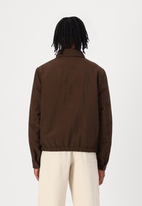Veste marron avec un col et un ourlet élastique. Fabriquée en tissu texturé, elle présente des poignets boutonnés et une coupe décontractée.