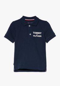 Námořnická modrá polokošile z bavlny, s třemi knoflíky po celé délce a logem "TOMMY HILFIGER" v bílé barvě na levém prsu. Krátké rukávy.
