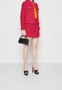 Ensemble de veste et jupe en vichy rose vif avec des boutons dorés, associé à un haut orange vif et un sac à main structuré noir. Talons plateformes noirs.