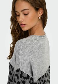 Grå tröja med en stickad textur, prydd med ett leopardskinnsmönster i svart. Plagget har en rund halsringning och sänkta axelsömmar.