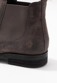 Brown suede ankle boot featuring elastic side panels, a flat black sole, and a subtle logo embossed on the heel.