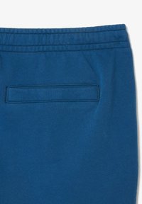 Pantalones de chándal azules con una cinturilla elástica y un bolsillo trasero plano con un contorno cosido. Textura suave con un acabado en color sólido.