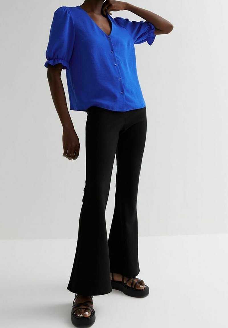 Blouse bleu à manches courtes avec un col en V et un devant à boutons, assortie à un pantalon noir évasé et des sandales noires à lanières. Texture lisse.