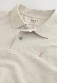 Béžová polo košeľa slim fit vyrobená z textúrovanej tkaniny, s gombíkovou légou a diskrétnym logom homára na ľavej strane.