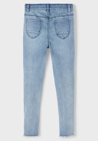 Jeans skinny de color azul claro en tejido de denim con una textura deslavada. Cuenta con una cintura de altura media y dos bolsillos traseros. Detalle de dobladillo deshilachado en los tobillos.